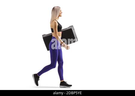 Photo de profil pleine longueur d'une jeune femme marchant et transport d'un stepper aérobie isolé sur fond blanc Banque D'Images