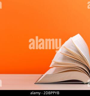 Un grand livre de couverture rigide épais repose sur une table en bois clair. Le livre est ouvert, les feuilles de la page sont défonsées, et le verso est un fond orange Banque D'Images