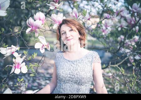 Cheerful senior femme arménienne dans une élégante robe en vertu de l'arbre en fleurs de magnolia. Banque D'Images