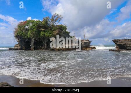 Des vagues se brisent sur une falaise au sommet de laquelle se trouve le temple hindou de Tanah Lot. Temple construit sur un rocher dans la mer au large de la côte de l'île de Bali, Indones Banque D'Images