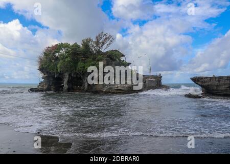 Des vagues se brisent sur une falaise au sommet de laquelle se trouve le temple hindou de Tanah Lot. Temple construit sur un rocher dans la mer au large de la côte de l'île de Bali, Indones Banque D'Images