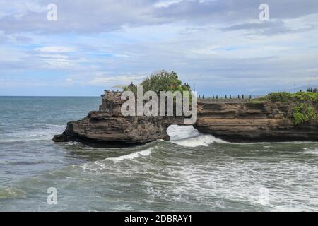 Les vagues arrivent sur une falaise au-dessous du temple de Batu Bolong. Temple Tanah Lot. Immense trou dans la falaise au-dessous du temple de Pura Batu Bolong. Temple hindou sur le be Banque D'Images