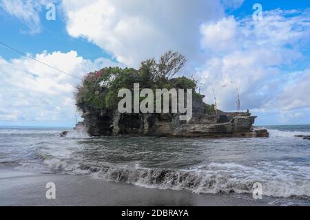 Des vagues se brisent sur une falaise au sommet de laquelle se trouve le temple hindou de Tanah Lot. Temple construit sur un rocher dans la mer au large de la côte de l'île de Bali, Indones Banque D'Images