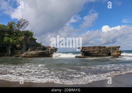 Des vagues se brisent sur une falaise au sommet de laquelle se trouve le temple hindou de Tanah Lot. Temple construit sur un rocher dans la mer au large de la côte de l'île de Bali, Indones Banque D'Images