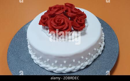 Le gâteau est recouvert de sugarpate blanche et décoré avec roses rouges Banque D'Images