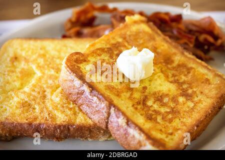 Deux morceaux de pain grillé sur une assiette blanche avec du bacon flou en arrière-plan. La dinde de beurre fond sur le dessus. Prise de vue. Banque D'Images