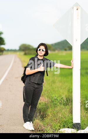 Young Asian woman cheveux courts et portant des lunettes de soleil avec sac à dos randonnée le long d'une route de campagne en Thaïlande Banque D'Images