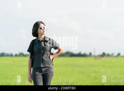 Young Asian woman cheveux courts et portant des lunettes de soleil avec sac à dos randonnée le long d'une route de campagne en Thaïlande Banque D'Images