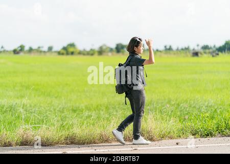 Young Asian woman cheveux courts et portant des lunettes de soleil avec sac à dos randonnée le long d'une route de campagne en Thaïlande Banque D'Images