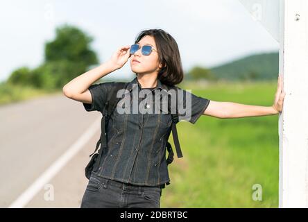 Young Asian woman cheveux courts et portant des lunettes de soleil avec sac à dos randonnée le long d'une route de campagne en Thaïlande Banque D'Images