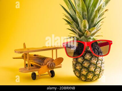 Célébrez le concept de la Journée des ananas d'été, ananas frais drôle dans des supports de lunettes de soleil avec un avion modèle, studio tourné isolé sur fond jaune, Holi Banque D'Images