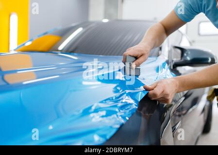 L'emballage de voiture, mécanique avec raclette, installe du film de protection en vinyle ou du film sur le capot du véhicule. L'employé effectue l'habillage automatique. Protection de peinture automobile Banque D'Images