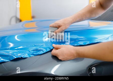 L'emballage de voiture, mécanique avec raclette, installe du film de protection en vinyle ou du film sur le capot du véhicule. L'employé effectue l'habillage automatique. Protection de peinture automobile Banque D'Images