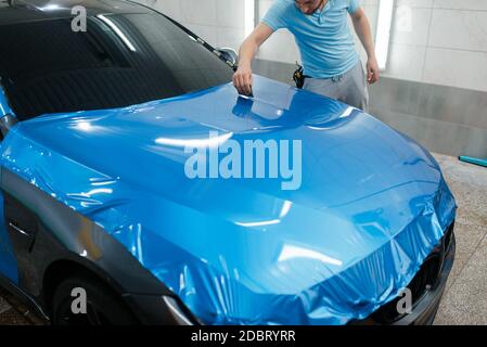 Emballage de voiture, homme avec raclette installe le film de protection en vinyle ou le film sur le capot. L'employé effectue l'habillage automatique. Revêtement de protection de peinture automobile, prof Banque D'Images