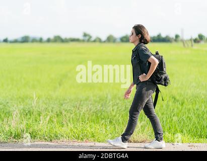 Young Asian woman cheveux courts et portant des lunettes de soleil avec sac à dos randonnée le long d'une route de campagne en Thaïlande Banque D'Images