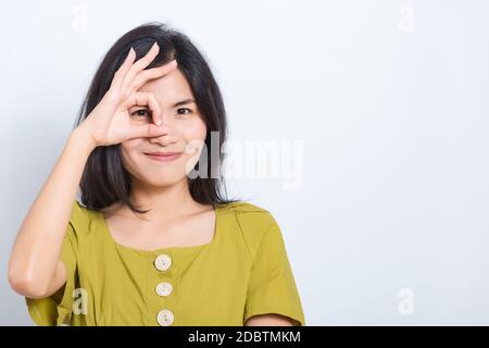 Portrait Asian belle jeune femme debout, elle a fait le doigt OK symbole signe pour convenir près de l'oeil et regarder l'appareil photo, prendre la photo en studio sur bleu b Banque D'Images