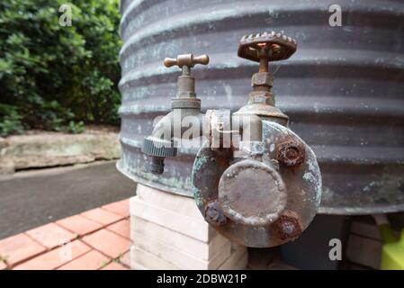 Un robinet extérieur en laiton relié à un ancien réservoir d'eau chaude en cuivre situé sur le toit, qui se trouve maintenant à l'extérieur et recueille l'eau de pluie sur un toit voisin Banque D'Images