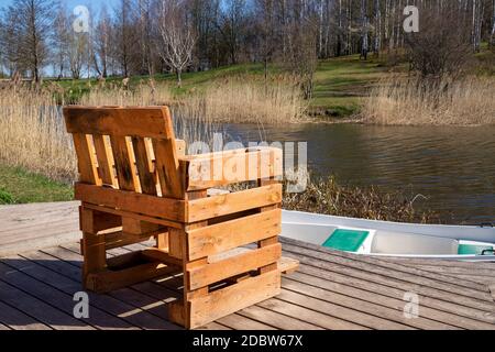 Chaise rustique faite à la main à partir de palettes en bois sur terrasse en bois donnant sur une rivière ou un lac avec des roseaux au soleil de printemps Banque D'Images