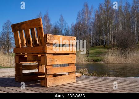 Chaise rustique faite à la main à partir de palettes en bois sur terrasse en bois donnant sur une rivière ou un lac avec des roseaux au soleil de printemps Banque D'Images