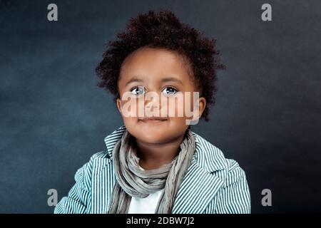 Portrait studio d'un petit garçon afro-américain élégant avec cheveux en boucle isolés sur fond sombre. Mode pour enfants. Vêtements pour enfants. Banque D'Images