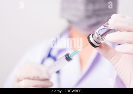 Femme asiatique médecin ou infirmière en uniforme et gants avec stéthoscope portant un masque de protection dans le laboratoire tenant la seringue et le médicament Banque D'Images