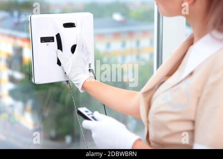 Une fille dans un uniforme contrôle un robot qui nettoie Windows. Vue depuis la fenêtre. Une photo méconnaissable. Vue latérale. Concept de nettoyage dans un hôtel ou Banque D'Images