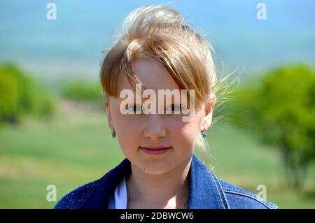 Portrait d'une fille blonde russe souriante de 10 ans sur fond de champ vert. Visage mignon, regardant l'appareil photo Banque D'Images