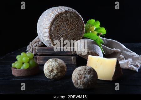 Têtes de fromage maison dur et raisins verts sur une serviette en lin sur fond sombre. Le concept de la vie encore. Copier l'espace. Banque D'Images