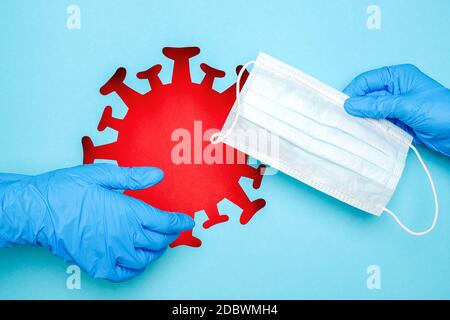 Deux mains en gants de latex et masque médical contre le coronavirus rouge, le virus, les bactéries, le microbe sur fond bleu. Concept créatif de protection Banque D'Images