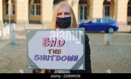 Femme inquiète dans un masque de protection avec une bannière de protestation appelant à terminez le shutdown en marchant dans la rue de la ville Banque D'Images