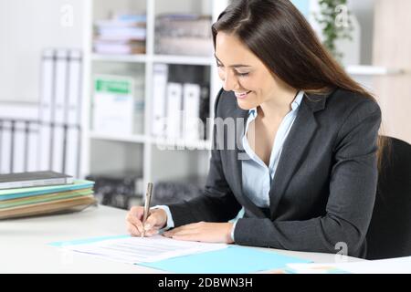 Une heureuse femme exécutive signe un contrat assis sur un bureau au bureau Banque D'Images