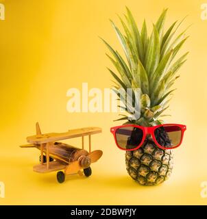 Célébrez le concept de la Journée des ananas d'été, ananas frais drôle dans des supports de lunettes de soleil avec un avion modèle, studio tourné isolé sur fond jaune, Holi Banque D'Images