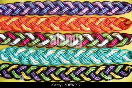 Sélection de multi-coloré tissé bricolage bracelets d'amitié Pigtail fait main de broderie fil brillant avec noeuds sur fond jaune Banque D'Images