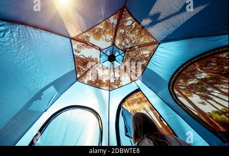 Femme au Camping bénéficie d'une belle vue sur la forêt à travers le filet transparent d'une tente. Vie touristique active. Banque D'Images