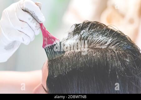 une jeune brune caucasienne mourant ses cheveux avec une brosse rose en utilisant des gants blancs à sa maison. Détails sur la brosse Banque D'Images