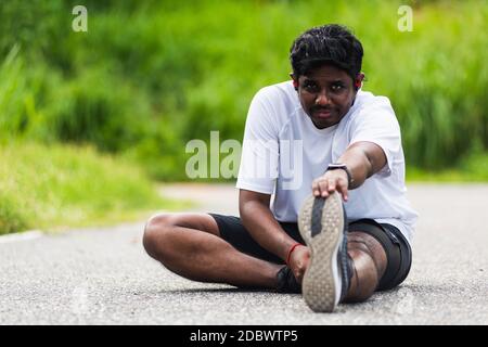 Gros plan asiatique jeune athlète coureur sportif noir homme porter montre il assis tirer les pieds étirement des jambes et des genoux avant de courir à l'extérieur de la rue guérir Banque D'Images