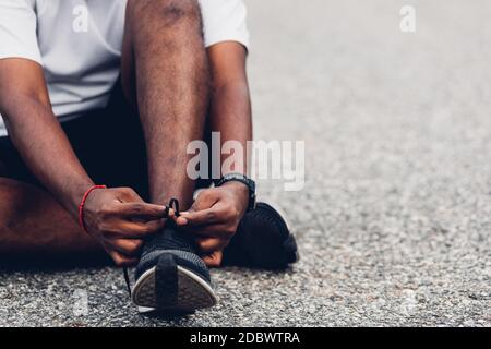 Gros plan asiatique coureur sportif noir homme assis chaussures de course à pied essayer des chaussures de course à pied se préparer pour le jogging et courir dans la rue extérieure, exercice de santé W Banque D'Images