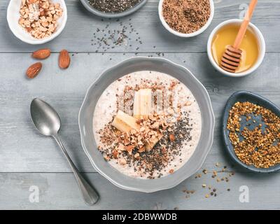 Du jour au lendemain de l'avoine dans un bol et les ingrédients - la banane, CVL, amandes et noix, amandes, miel et pollen gris sur fond de table en bois. Petit-déjeuner sain d'avoine Banque D'Images