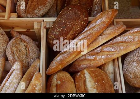 Gros plan sur plusieurs pains de blé frais assortis et baguettes dans une boîte en bois sur l'affichage au détail d'un magasin de boulangerie, vue en grand angle Banque D'Images