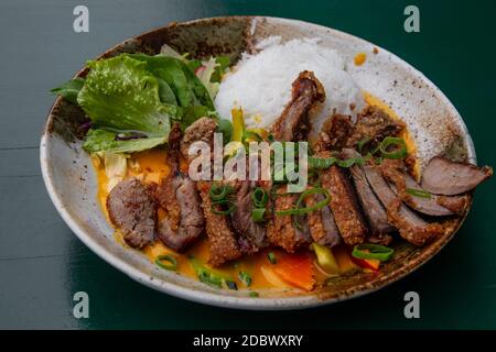 Close up partie de tranches de rôti, croustillant de canard de Pékin curry avec riz et salade sur plaque sur table, high angle view Banque D'Images