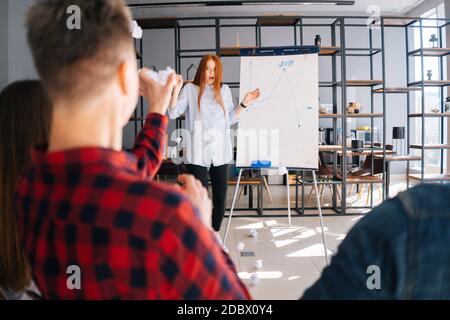 REDHEAD Business Woman finissant le rapport sur le tableau. Des collègues mécontents lancent des boules de papier froissés Banque D'Images