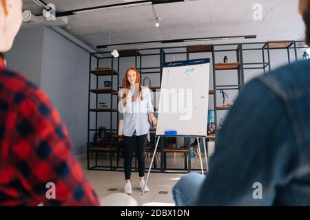 REDHEAD Business Woman finissant le rapport sur le tableau. Des collègues mécontents lancent des boules de papier froissés Banque D'Images