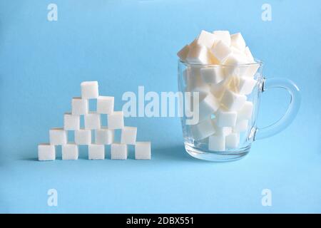 Tasse transparente pleine de cubes de sucre blanc raffiné et pyramide faite de cubes de sucre blanc sur fond bleu. Copier l'espace Banque D'Images