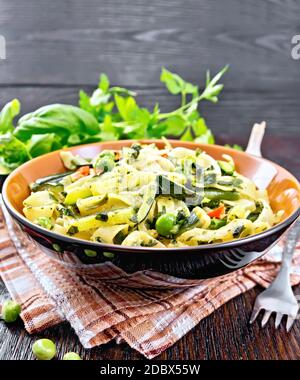 Pâtes tagliatelles avec courgettes, petits pois, haricots asperges, poivrons chauds et épinards dans une assiette sur serviette brune, ail, fourchette et basilic sur sanglier Banque D'Images