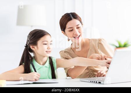 Mère avec fille regardant l'ordinateur portable et travaillant à la maison Banque D'Images