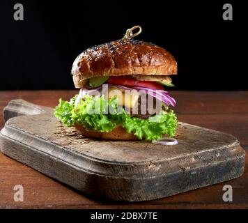 délicieux hamburgers avec côtelettes de bœuf frites, tomate, laitue et oignons, pain croustillant à la farine de blé blanc aux graines de sésame. Restauration rapide sur une planche de bois, dessus Banque D'Images