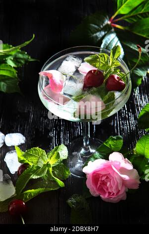 Limonade dans un grand verre avec baies de cerise et pétales de rose. Photo verticale sur fond noir. Vue de dessus. Banque D'Images