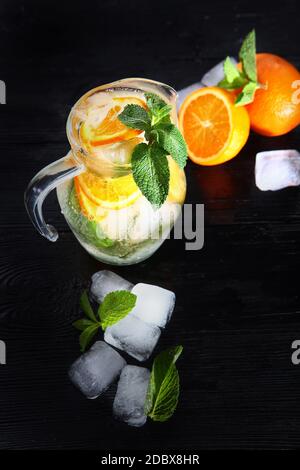 Limonade fraîche à base d'oranges et de menthe dans une verseuse en verre. Glaçons dans la boisson. Copier l'espace. Photo verticale sur fond noir.vue du dessus. Banque D'Images