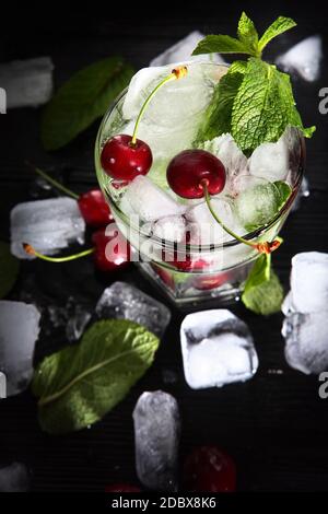 Refroidir la limonade à la cerise dans un verre avec de la glace et de la menthe. Feuilles de menthe dans un verre. Boisson d'été en saison. Photo sur fond noir. Vue de dessus. Banque D'Images