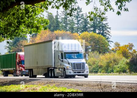 Convoi de deux engins de forage semi de qualité industrielle différents chariots tracteurs avec remorques sèches et semi-remorques à conteneurs en marche sur la route d'été avec g Banque D'Images